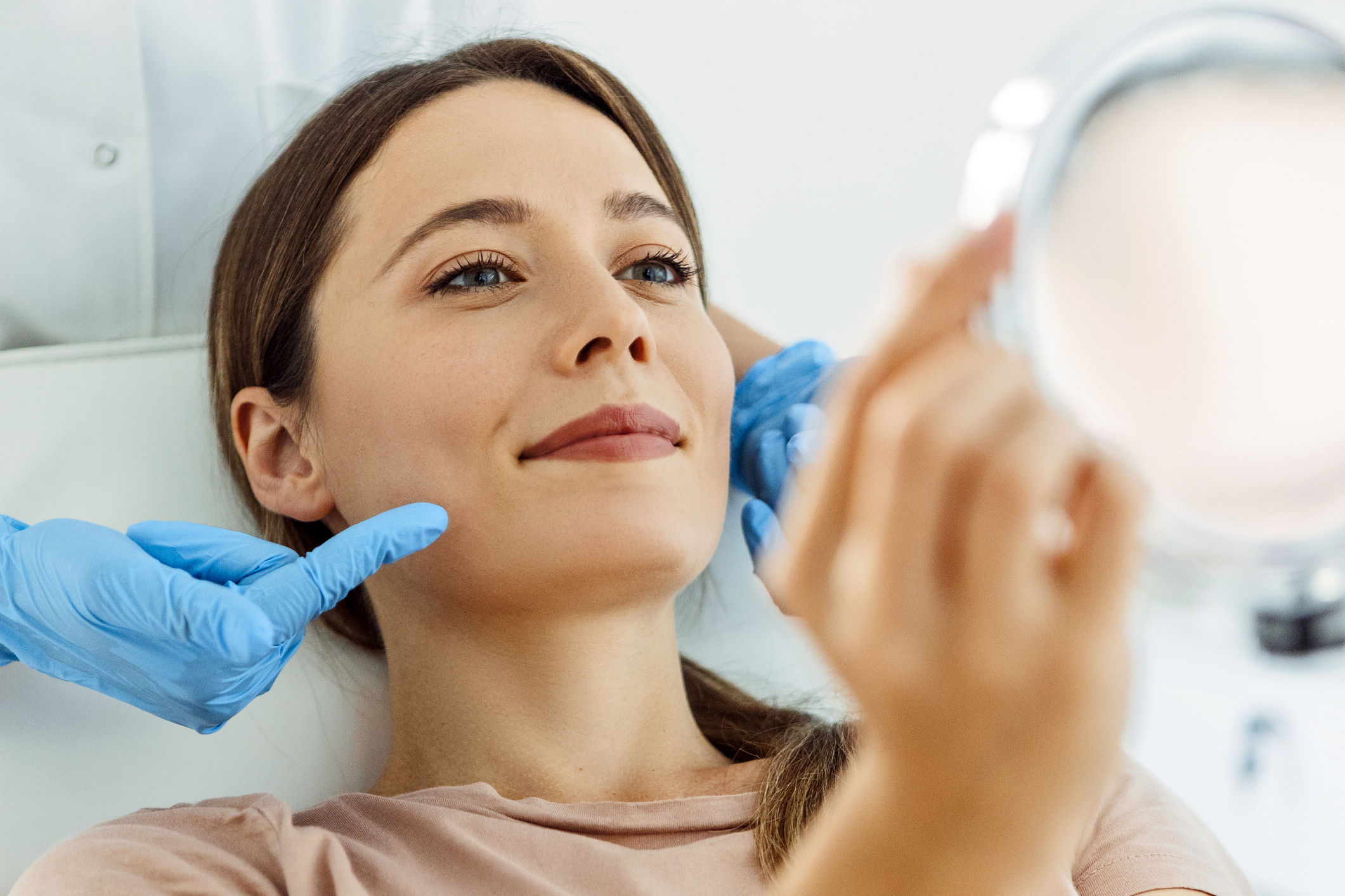 Woman checking her smile in a hand mirror after treatment